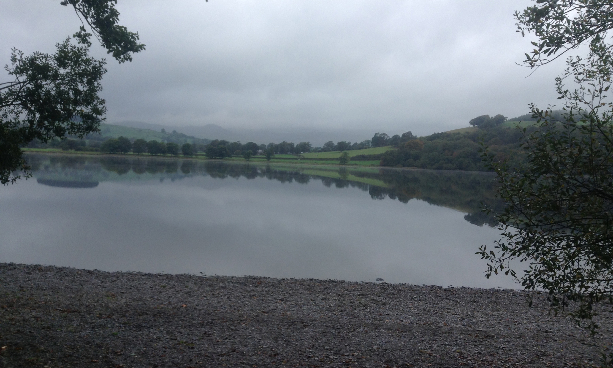 Grey sky, the green hills reflected in the still waters of the lake